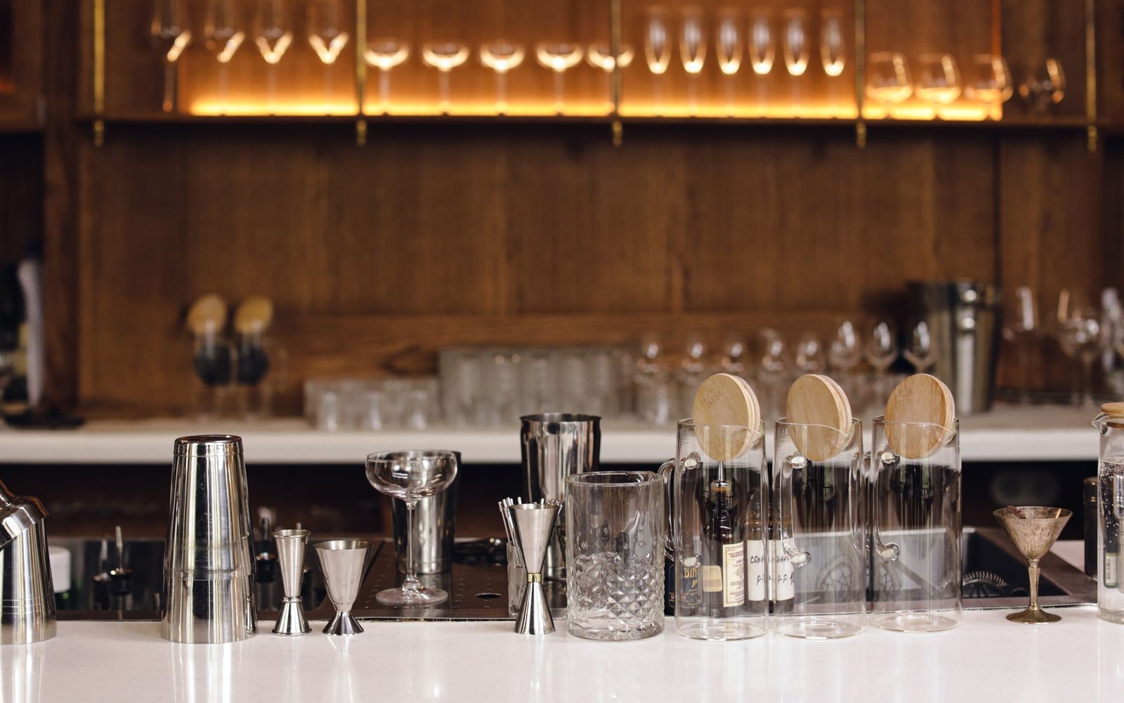 Wide shot of a bar surface mid-evening: coasters, glassware, a few bottles in the foreground — the kind of still life that tells you where you are bef