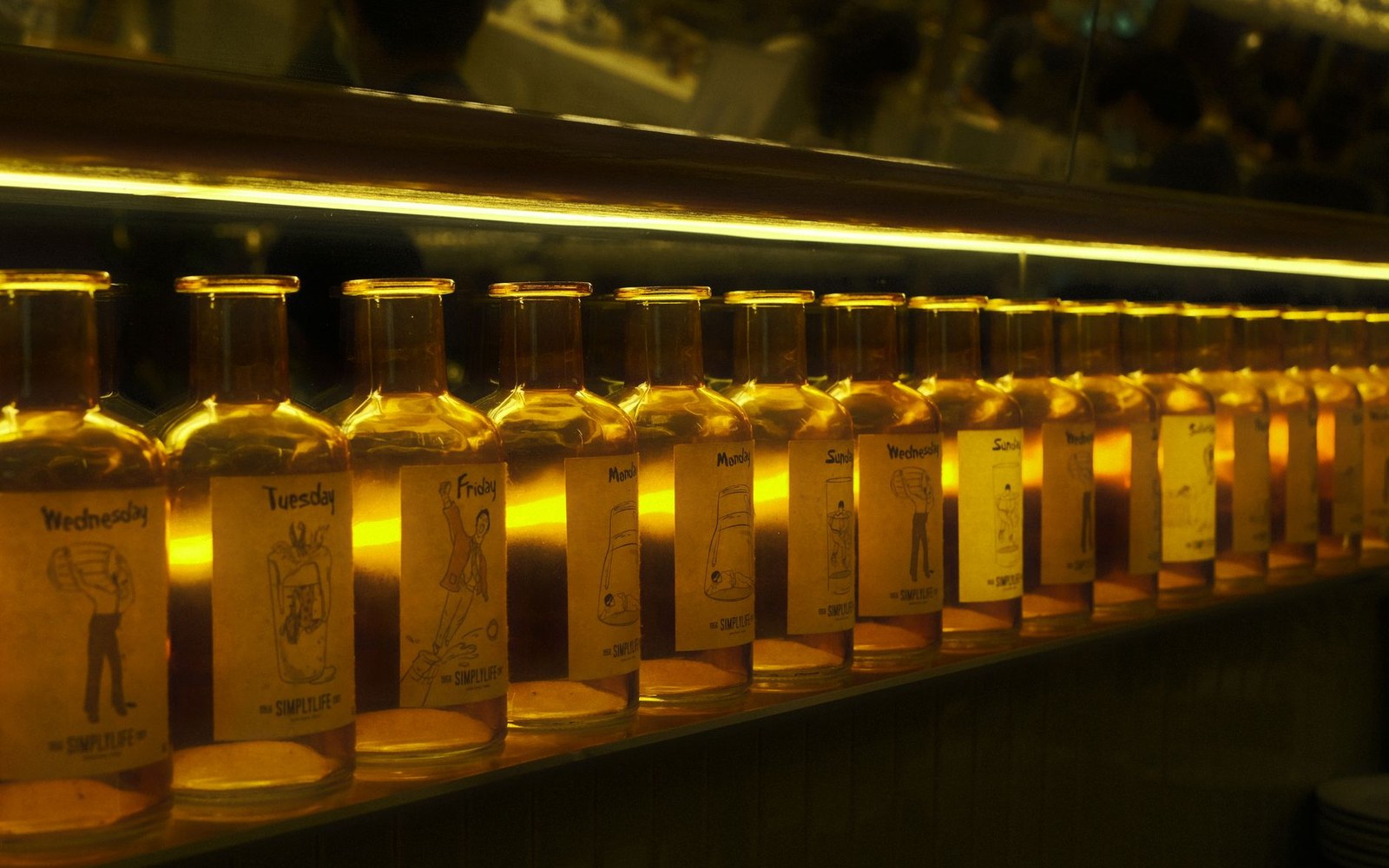 A dim back bar, rows of bottles ranked against a low mirror, lit from below by a single strip