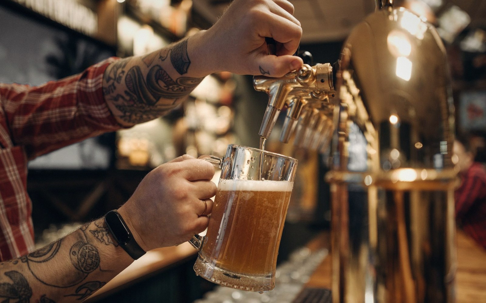 A bartender's hands mid-pour, forearms only, bar rail and rail mats visible below