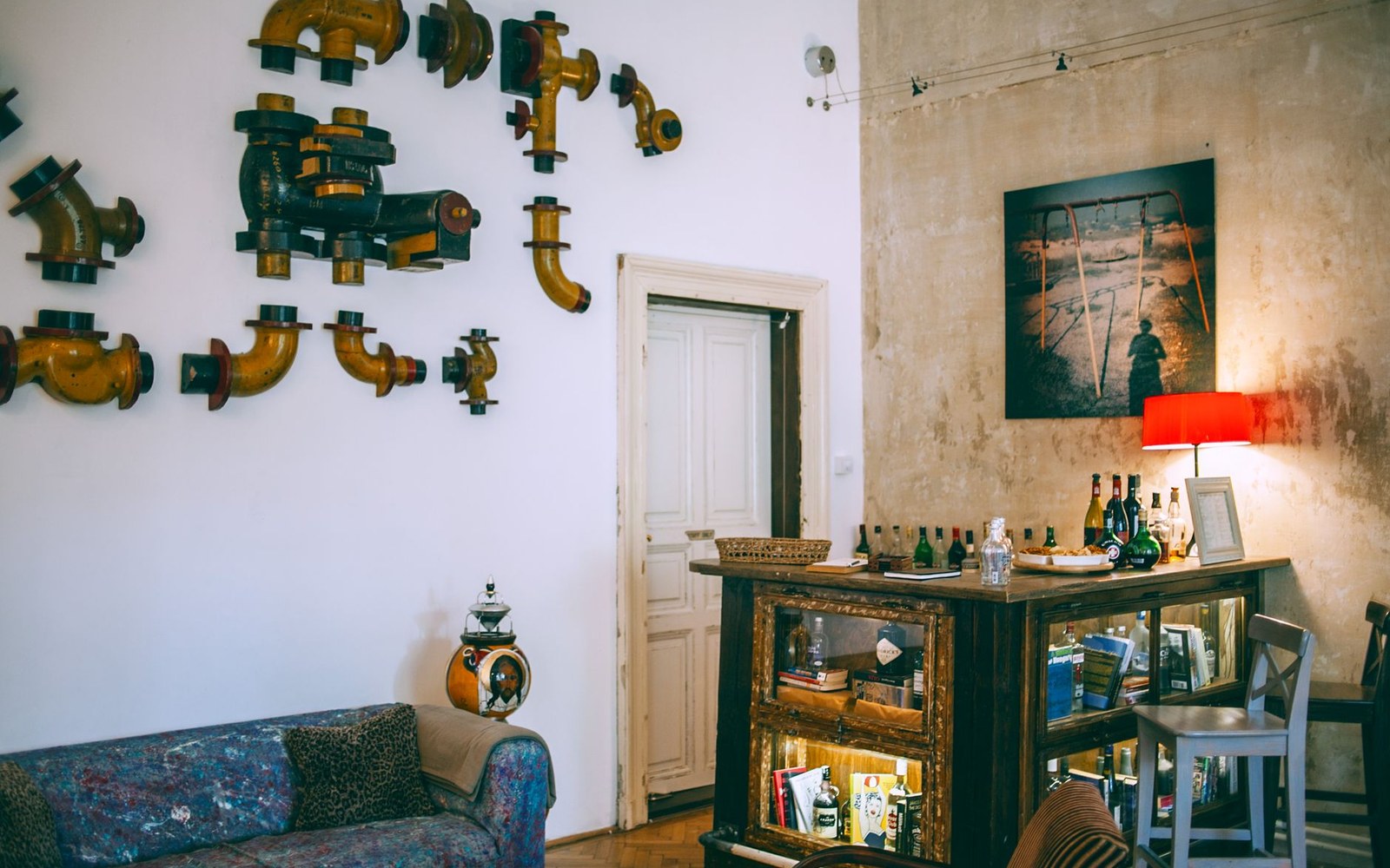 Vintage pipe fittings decorate a wall above a worn sofa and glass display cabinet