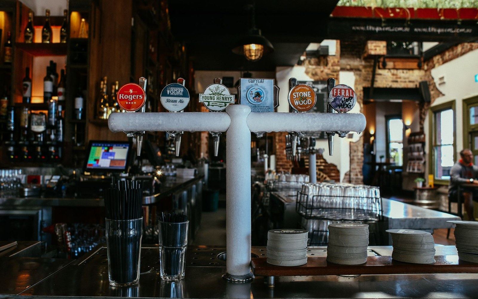 Row of craft beer taps lined up on a bar counter with coasters and glasses nearby