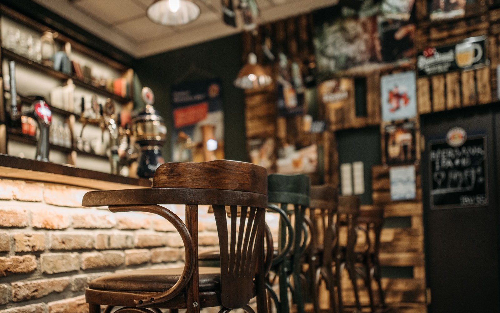 Wooden bentwood chairs line a brick-walled bar with beer taps and posters