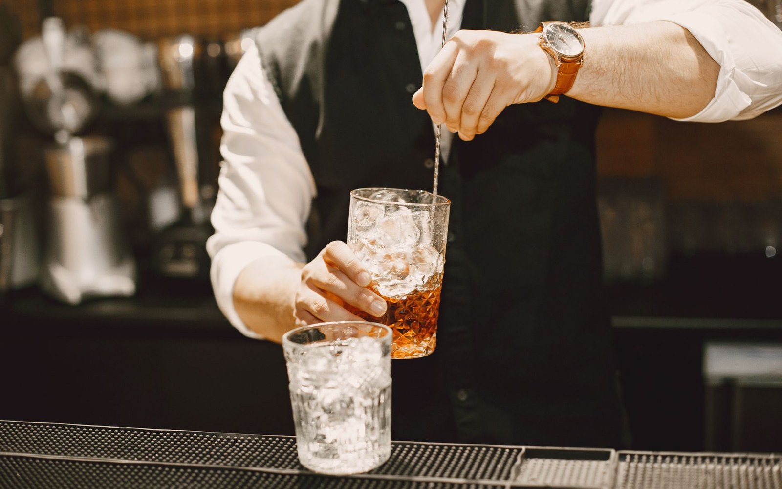 Bartender stirs an amber cocktail over ice with a bar spoon