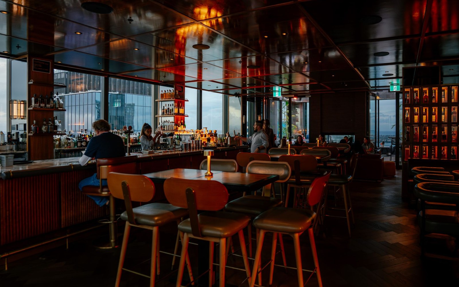 High-rise bar with tall windows overlooking a city skyline at dusk