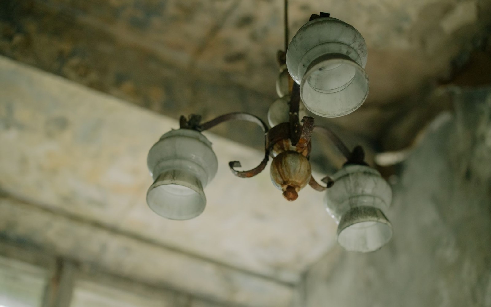 A rusted ceiling light fixture with grimy glass shades in an abandoned room