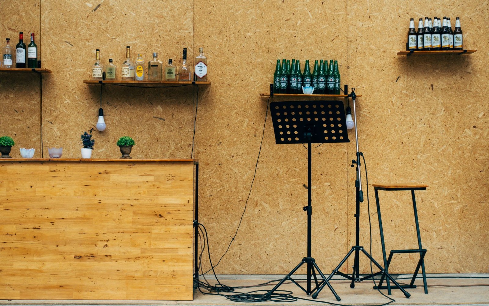 Wooden bar with liquor shelves beside a music stand, microphone and stool on a small stage