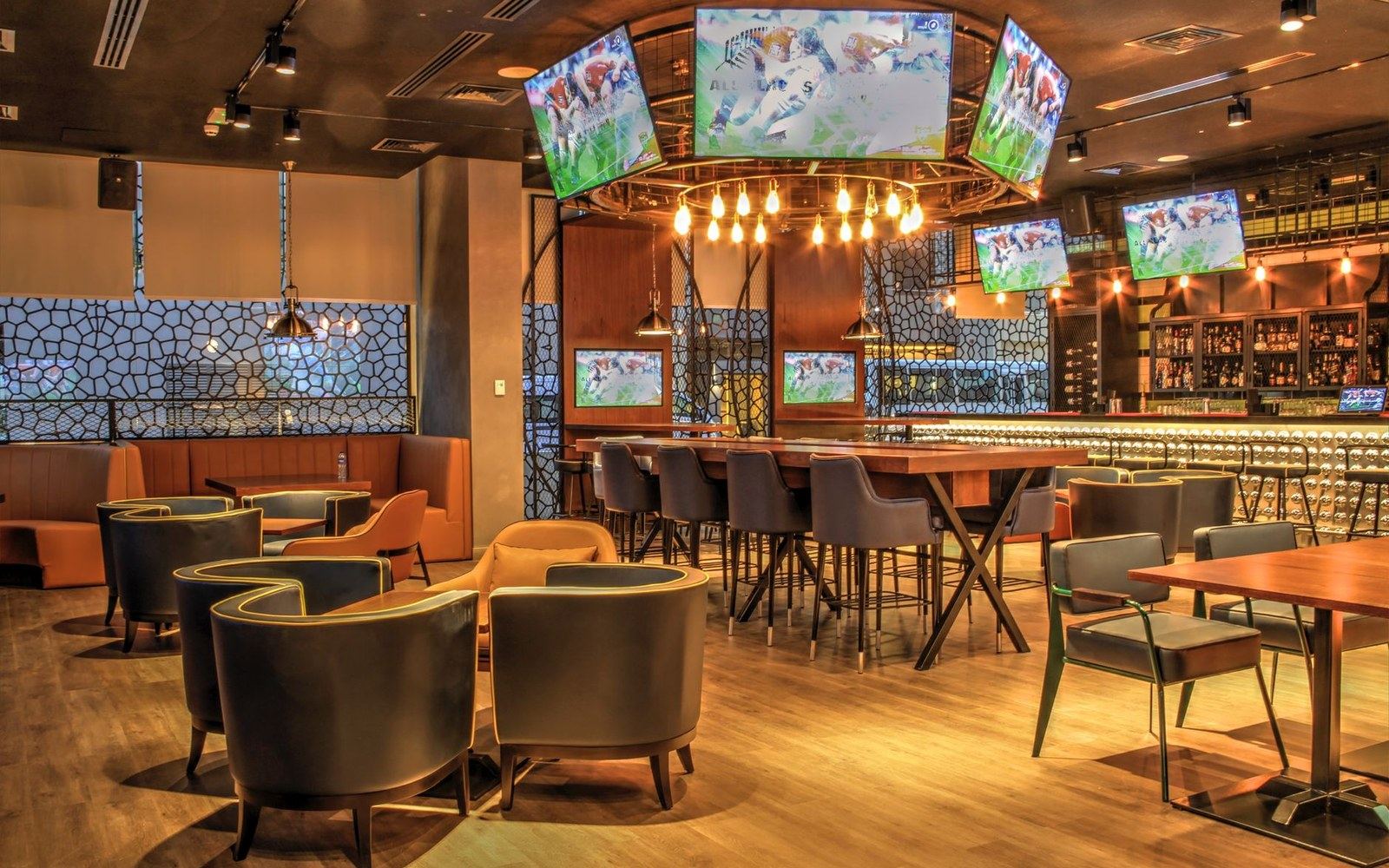 Sports bar interior with hanging televisions, a bulb chandelier, and leather lounge seating