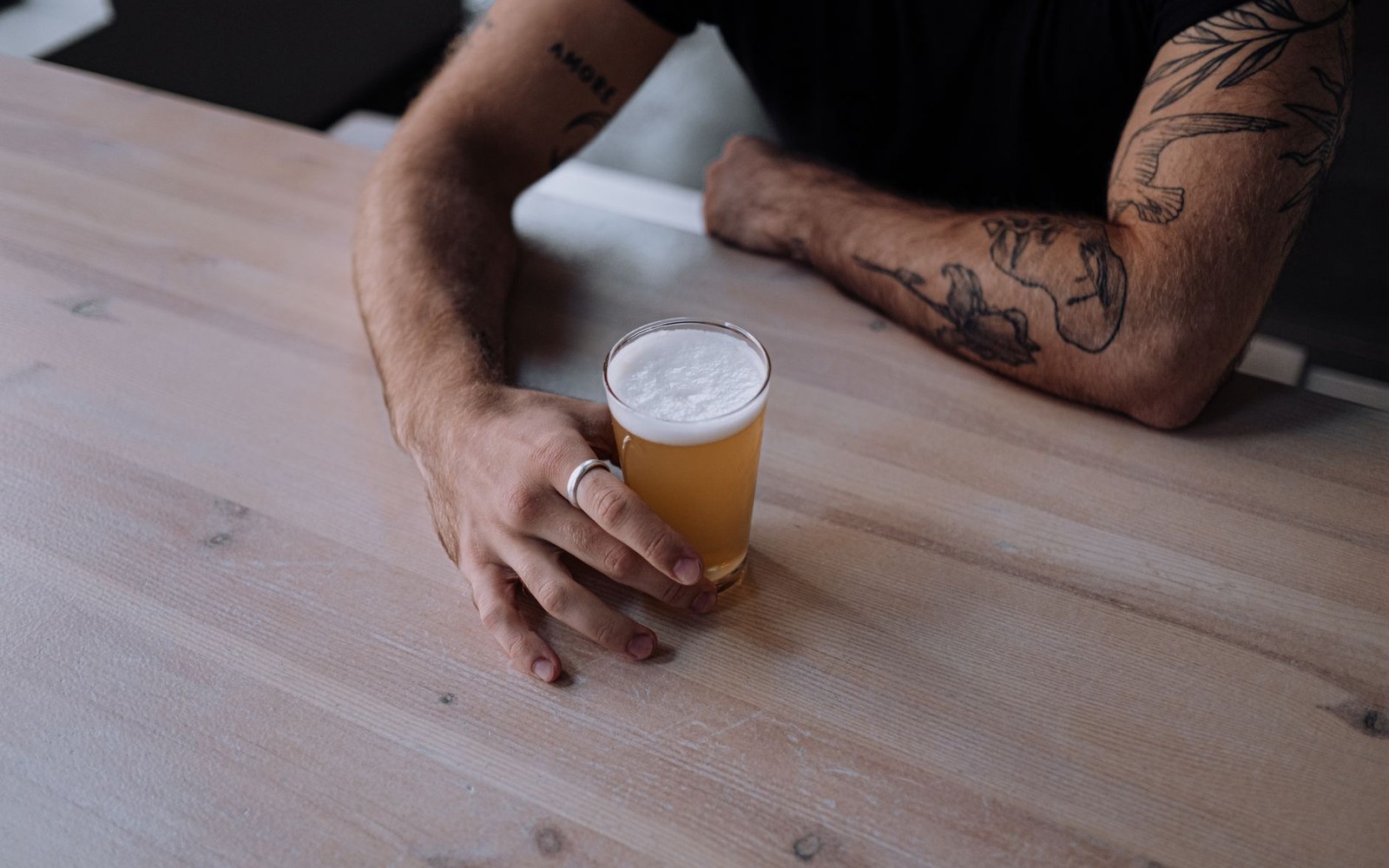 A pale beer mid-settle in a straight glass, condensation on the outside, on a dark bar surface